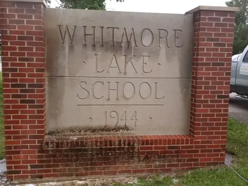 The algae-stained Whitmore Lake School 1944 stone landmark sign, then the same sign cleaned