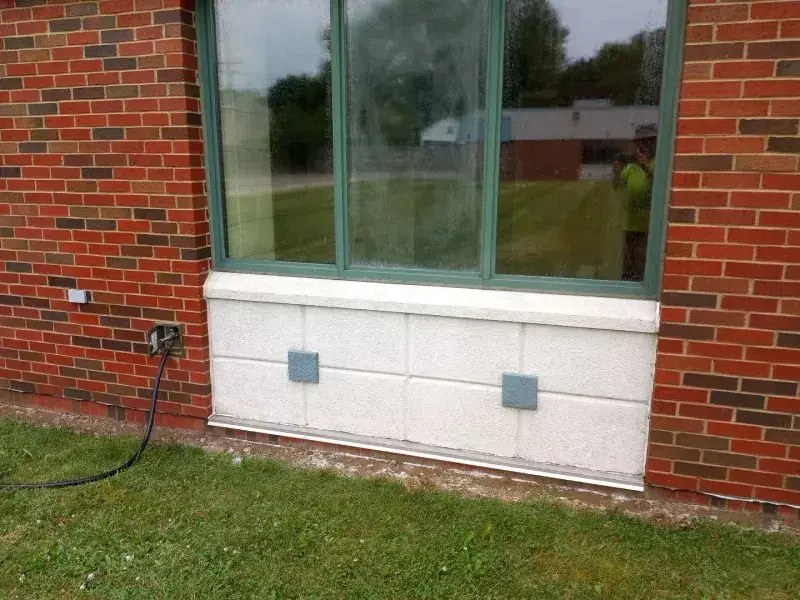 A dirty brick commercial building sill with a worker reflected in the glass, then the same sill cleaned
