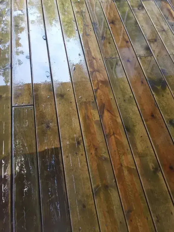 A wooden deck half cleaned and half still dirty, with water pooled on the finished side